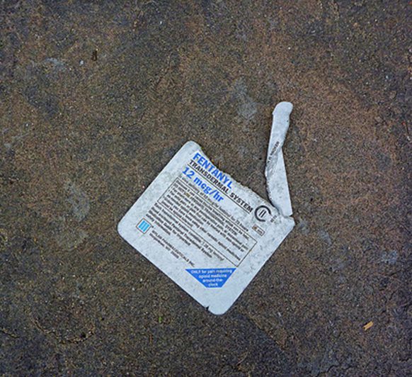 A piece of paper on the ground with a broken razor blade.
