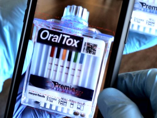 A person holding an iphone with a box of oral tox.