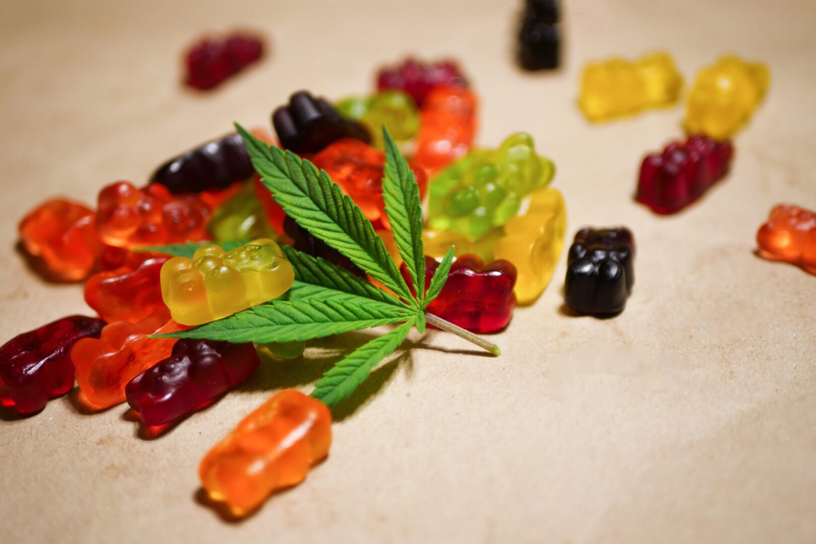A pile of gummy bears with marijuana leaves on top.